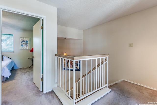 corridor featuring an upstairs landing, carpet flooring, a textured ceiling, and baseboards