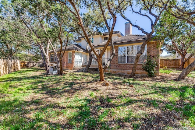 back of property featuring a yard, brick siding, a fenced backyard, and a chimney