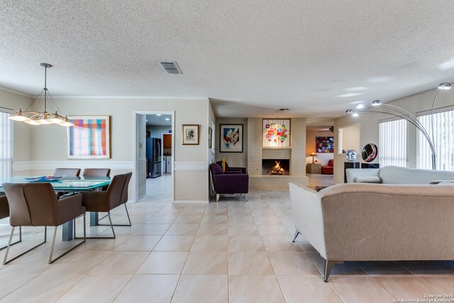 living area featuring visible vents, a brick fireplace, crown molding, light tile patterned flooring, and a textured ceiling