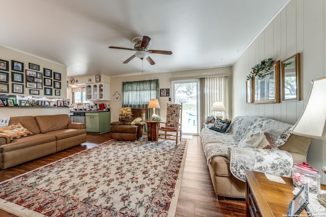 living room with dark wood-type flooring, a ceiling fan, and crown molding