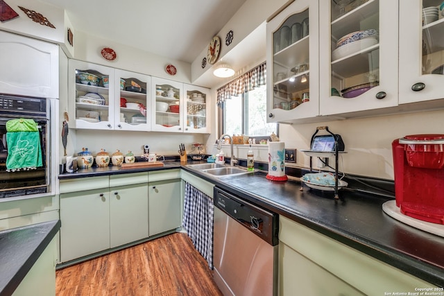 kitchen featuring wood finished floors, a sink, dishwasher, dark countertops, and black oven