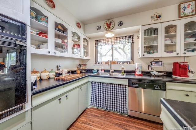 kitchen featuring oven, a sink, stainless steel dishwasher, dark countertops, and wood finished floors