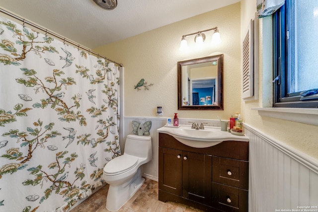 full bathroom featuring a shower with curtain, vanity, toilet, and wainscoting