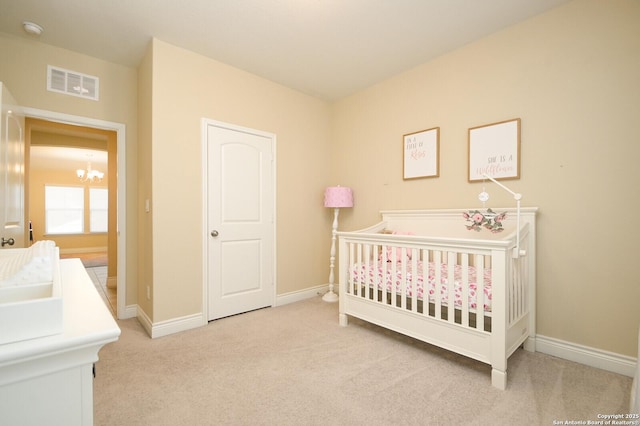 carpeted bedroom featuring a crib, baseboards, visible vents, and a chandelier
