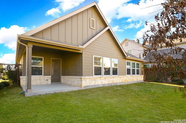 rear view of house with a patio area, a lawn, board and batten siding, and stone siding