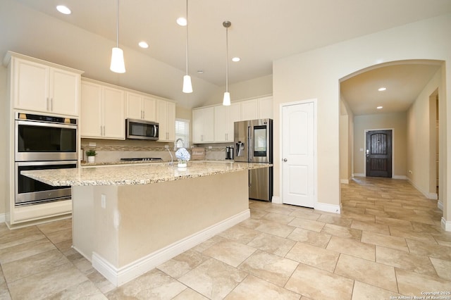 kitchen with an island with sink, light stone counters, arched walkways, appliances with stainless steel finishes, and white cabinets