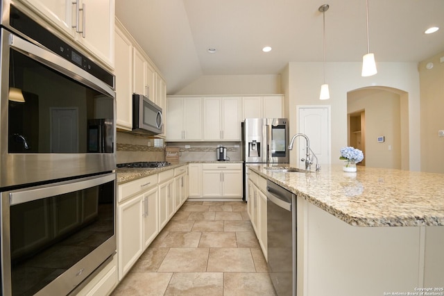 kitchen featuring backsplash, stainless steel appliances, arched walkways, white cabinetry, and a sink