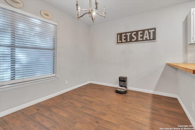 spare room with baseboards, wood finished floors, and a chandelier