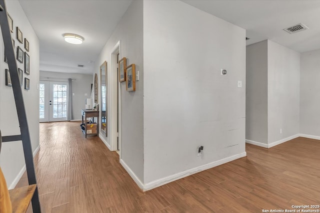 corridor featuring french doors, baseboards, visible vents, and wood finished floors