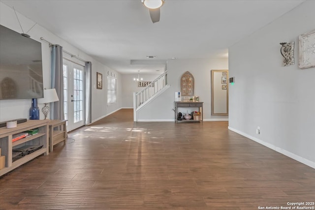 unfurnished living room featuring ceiling fan with notable chandelier, stairway, wood finished floors, and baseboards