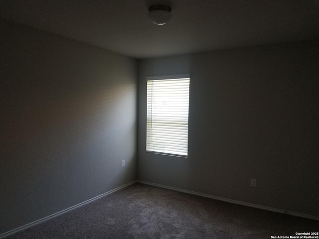 spare room with baseboards and dark carpet