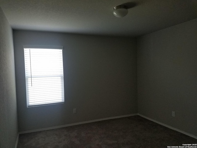 empty room featuring a wealth of natural light, baseboards, and dark colored carpet