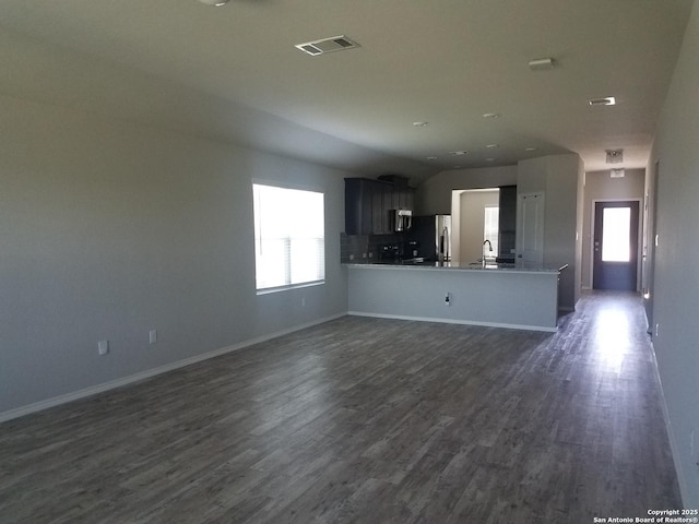 unfurnished living room featuring dark wood-style flooring, visible vents, a wealth of natural light, and a sink