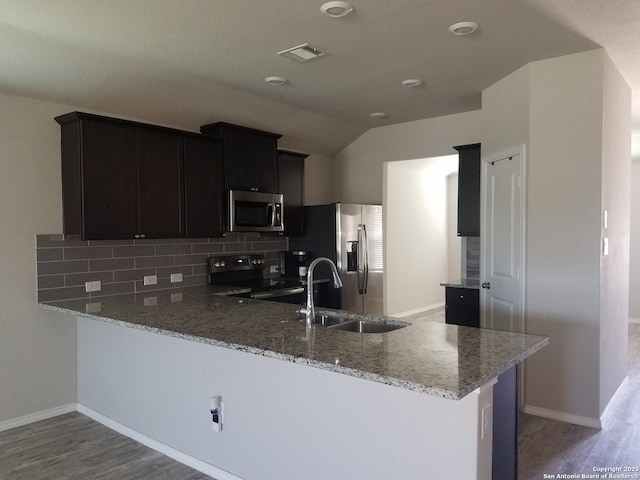 kitchen with backsplash, light stone countertops, a peninsula, stainless steel appliances, and a sink