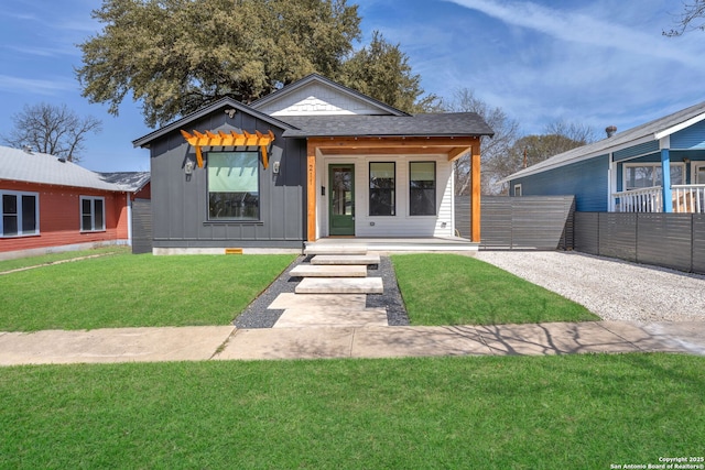 view of front of home featuring board and batten siding, roof with shingles, a front lawn, and fence