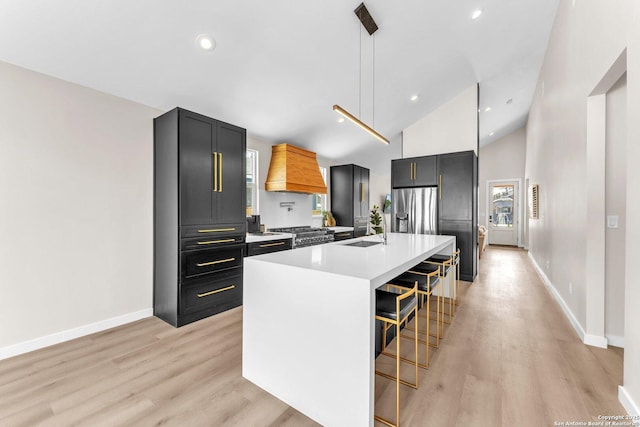 kitchen featuring premium range hood, a sink, light wood-style floors, a breakfast bar area, and light countertops