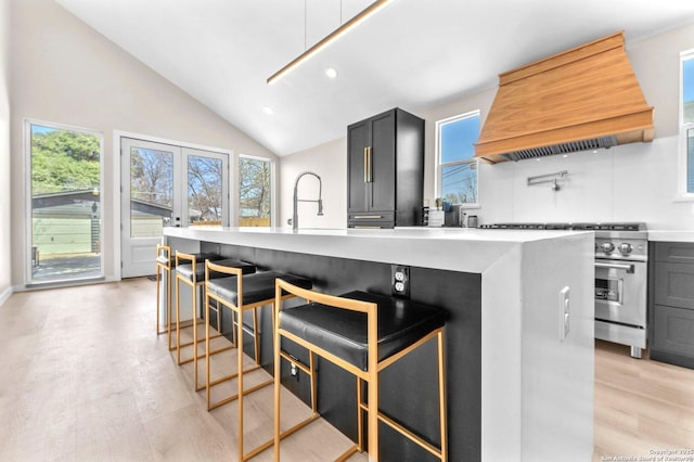 kitchen with lofted ceiling, stainless steel range, custom range hood, light countertops, and light wood-style floors