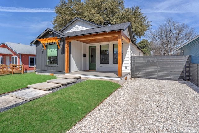 view of front facade with roof with shingles, board and batten siding, a front lawn, and fence