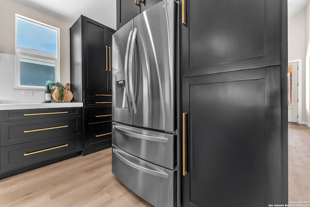 kitchen featuring dark cabinetry, light wood-style flooring, stainless steel refrigerator with ice dispenser, and light countertops