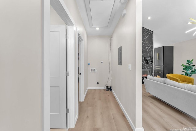 hall with attic access, light wood-style flooring, electric panel, and baseboards