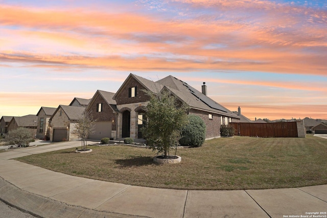french country inspired facade with roof mounted solar panels, fence, a yard, concrete driveway, and an attached garage