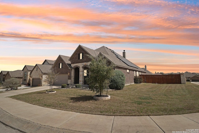 french provincial home with fence, concrete driveway, roof mounted solar panels, a yard, and an attached garage