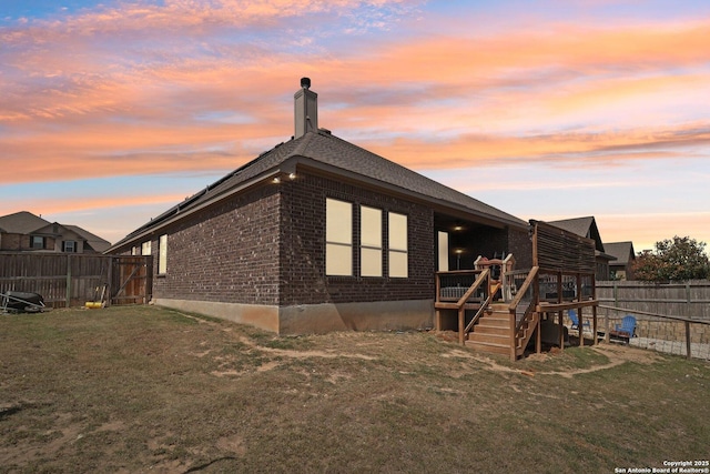 exterior space featuring fence, a yard, a chimney, a deck, and brick siding