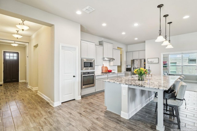 kitchen with visible vents, appliances with stainless steel finishes, a center island with sink, and light wood finished floors