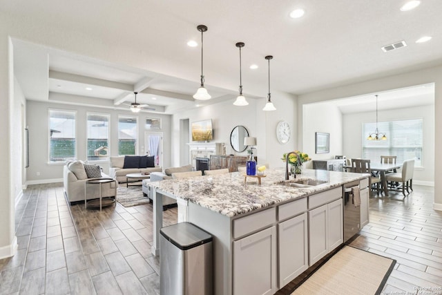 kitchen featuring pendant lighting, a center island with sink, a sink, light stone counters, and stainless steel dishwasher