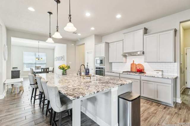 kitchen with tasteful backsplash, a sink, a kitchen bar, appliances with stainless steel finishes, and a kitchen island with sink