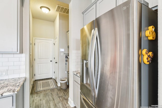 kitchen featuring light stone countertops, visible vents, stainless steel fridge with ice dispenser, light wood-style floors, and tasteful backsplash