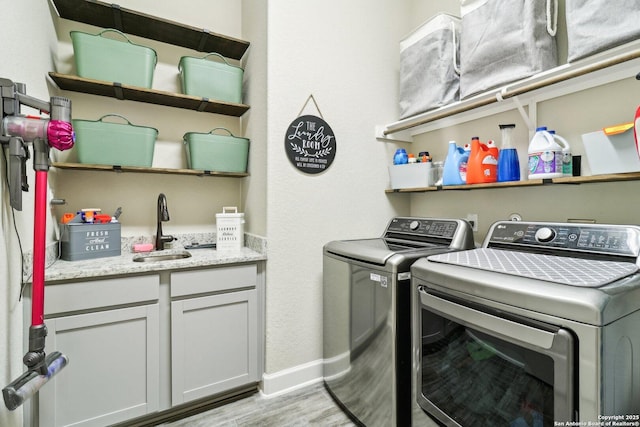 clothes washing area featuring independent washer and dryer, light wood-style flooring, a sink, cabinet space, and baseboards