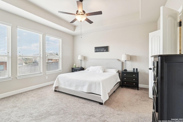 bedroom with light carpet, baseboards, a tray ceiling, and a ceiling fan