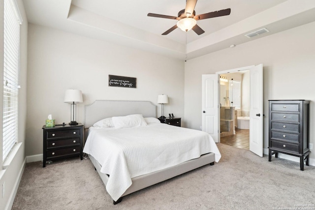 bedroom with connected bathroom, carpet, a tray ceiling, and ceiling fan