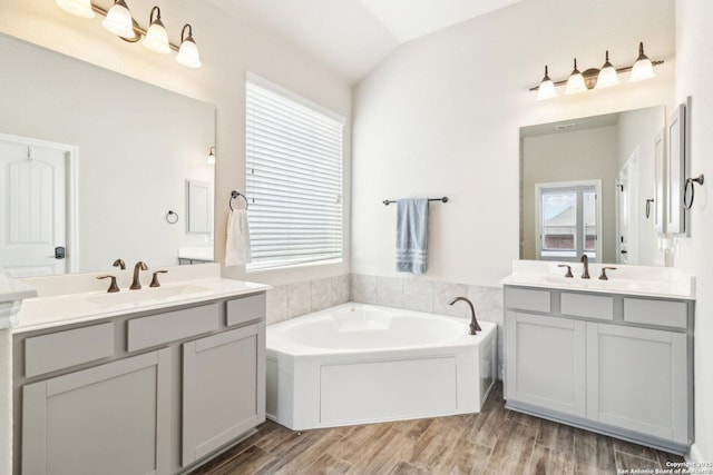 bathroom featuring vaulted ceiling, a bath, wood finished floors, and a sink