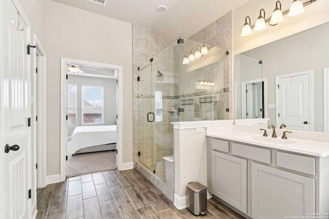 ensuite bathroom featuring wood finish floors, a stall shower, ceiling fan, vanity, and vaulted ceiling