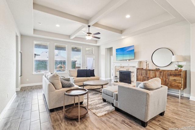 living room featuring beamed ceiling, coffered ceiling, wood finished floors, a stone fireplace, and baseboards