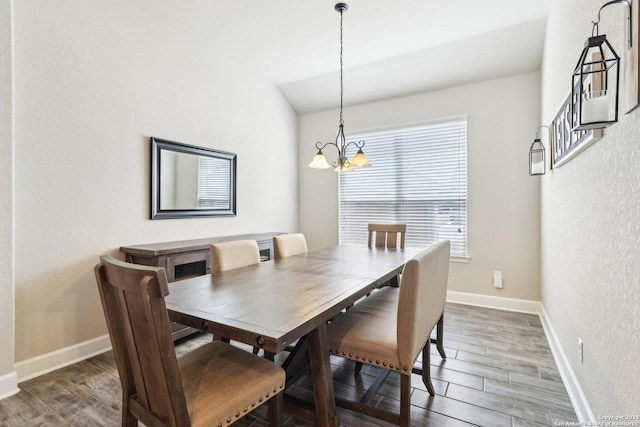 dining space featuring vaulted ceiling, a notable chandelier, baseboards, and wood finished floors