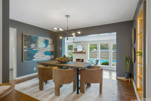 dining room with a brick fireplace, baseboards, ceiling fan, and wood finished floors