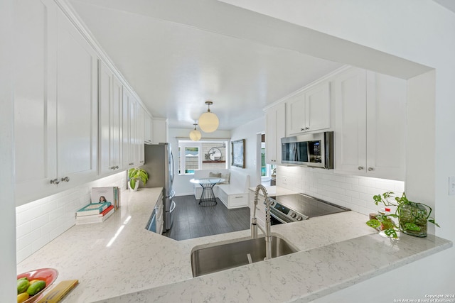 kitchen with light stone counters, decorative backsplash, white cabinets, stainless steel appliances, and a sink