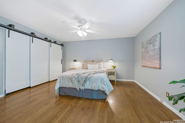 bedroom with ceiling fan, baseboards, a barn door, and wood finished floors