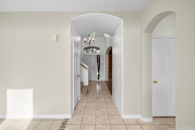 corridor with light tile patterned floors, an inviting chandelier, arched walkways, and baseboards