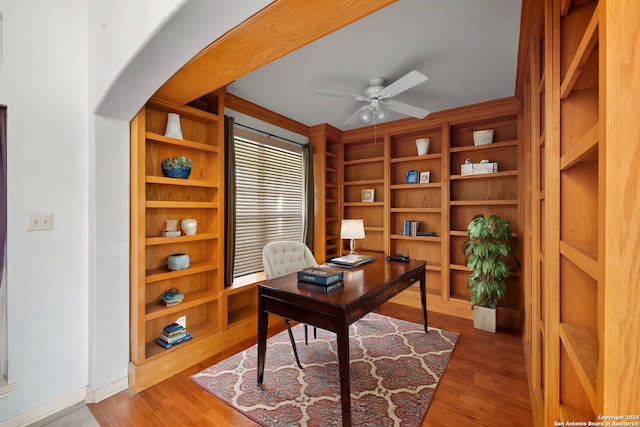 office featuring baseboards, wood finished floors, arched walkways, and ceiling fan