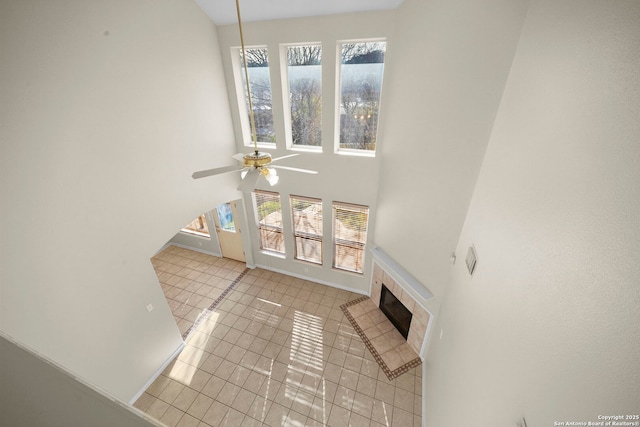 tiled living room with ceiling fan, baseboards, a towering ceiling, and a tile fireplace