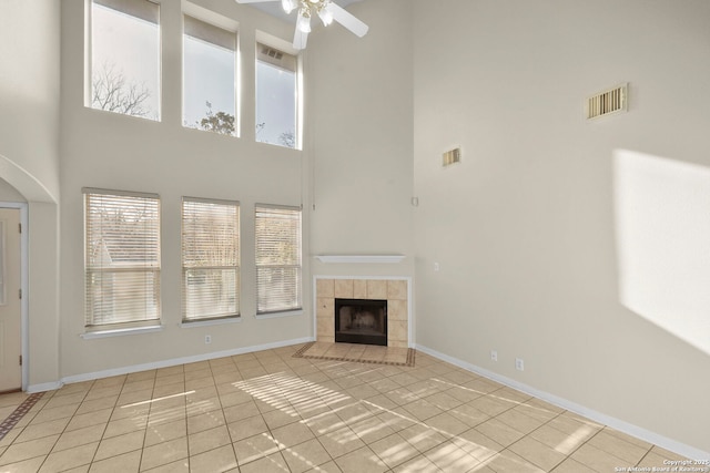 unfurnished living room featuring a tiled fireplace, a ceiling fan, visible vents, and baseboards