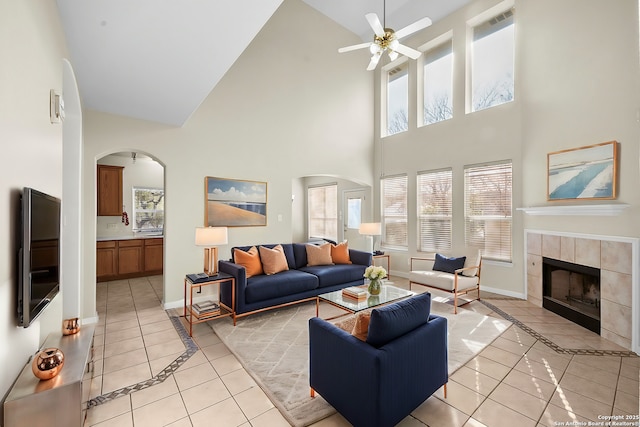 living area featuring arched walkways, a fireplace, ceiling fan, and light tile patterned flooring