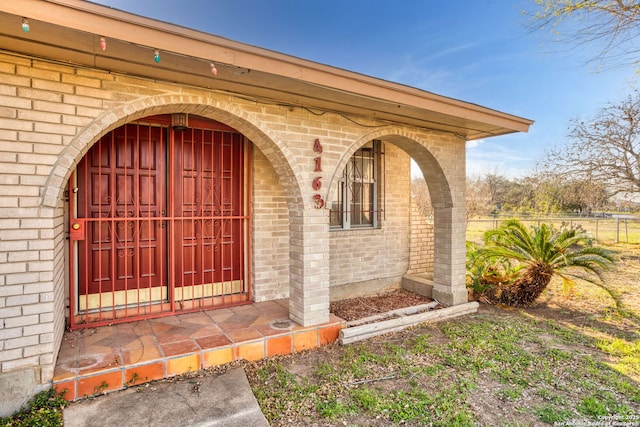 doorway to property with brick siding and fence