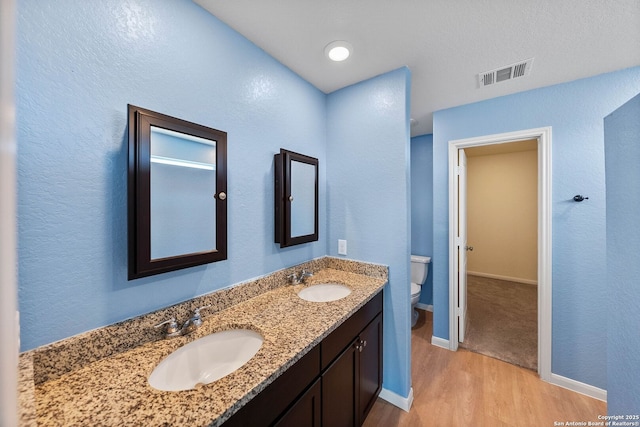 full bath featuring toilet, wood finished floors, visible vents, and a sink