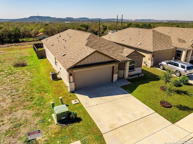 view of front of property featuring an attached garage, a front yard, central AC unit, driveway, and a mountain view