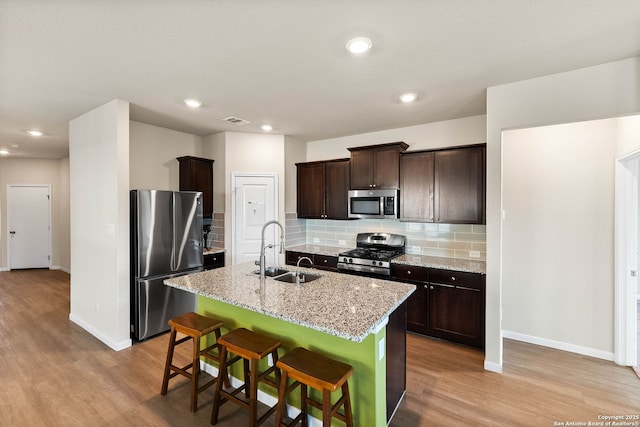 kitchen featuring dark brown cabinetry, appliances with stainless steel finishes, light wood-style floors, and a sink